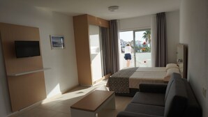 Habitación de hotel con cama, sofá, televisión, banca y balcón con vista a la ciudad.