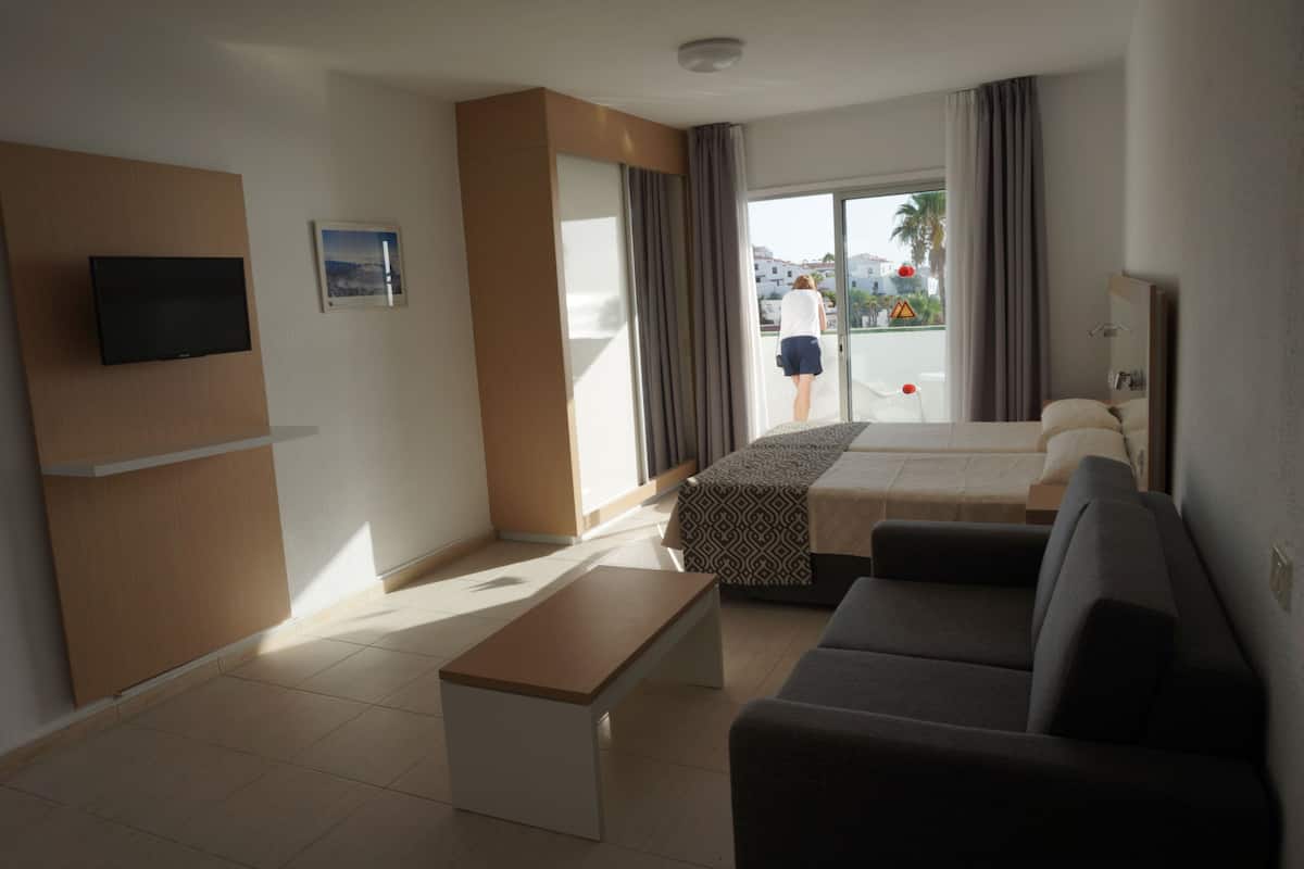Ett hotellrum med en säng, en soffa, en tv, en bänk och en balkong med utsikt över staden.