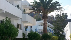 Un edificio moderno con paredes exteriores blancas, balcones y una palmera en el centro.