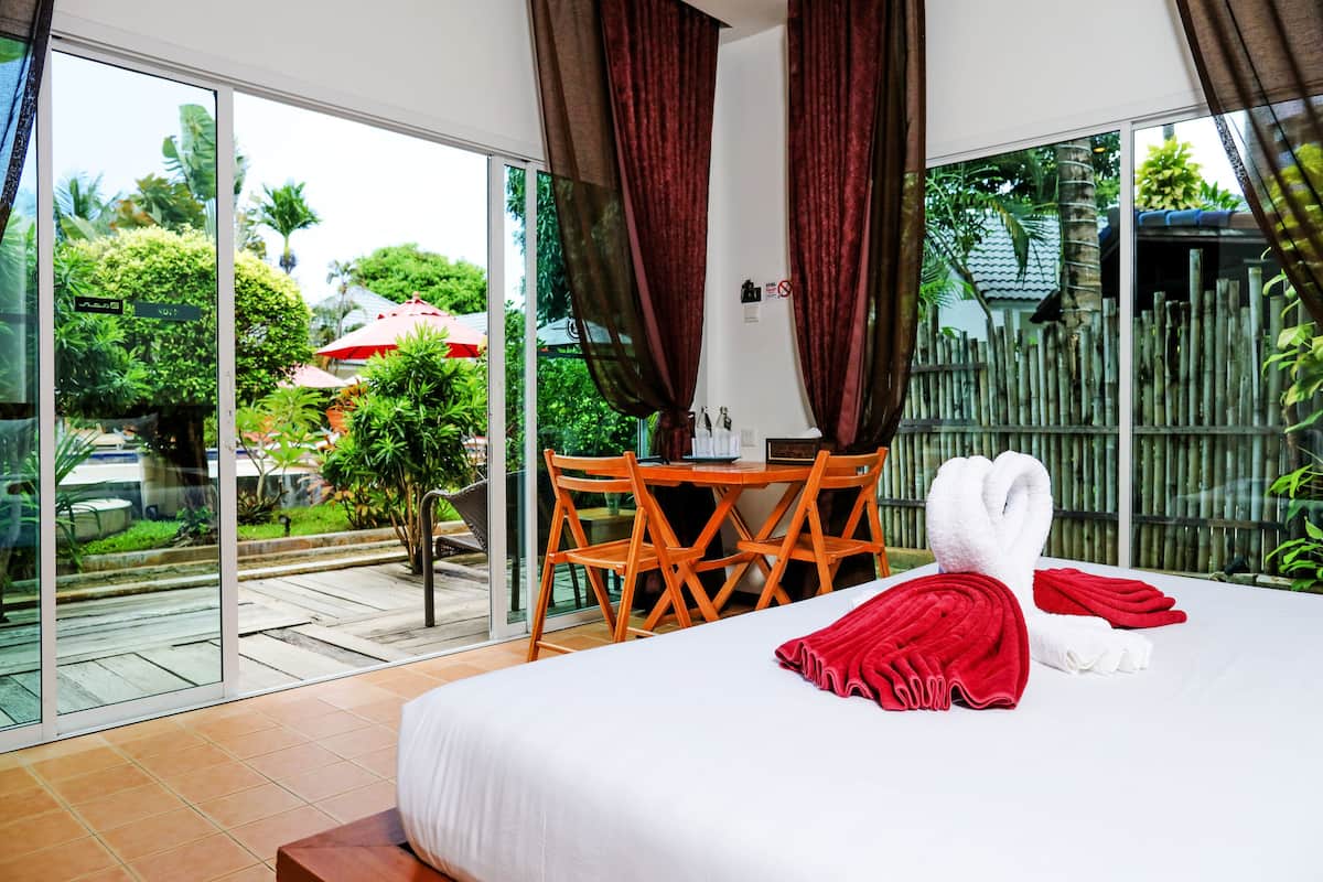 A hotel room with a large bed, a wooden table with chairs, and a view of a garden through large sliding doors.