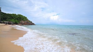 A beach with clear water, sandy shore, and a forested cliff. - Bhumlapa Garden Resort (Koh Samui)