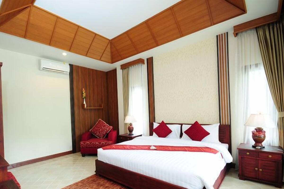 A bedroom with a large bed, wooden ceiling, and a red accent wall.