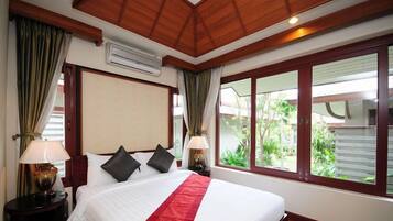 A hotel room with a large bed, two bedside lamps, a red bedspread, and a view of greenery outside.