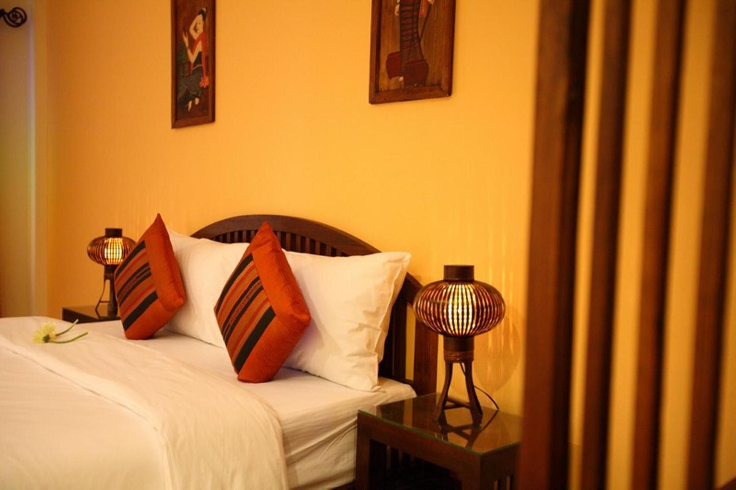 A neatly made bed with white linens and striped pillows, a bedside table with a lamp, and two wall-mounted paintings.