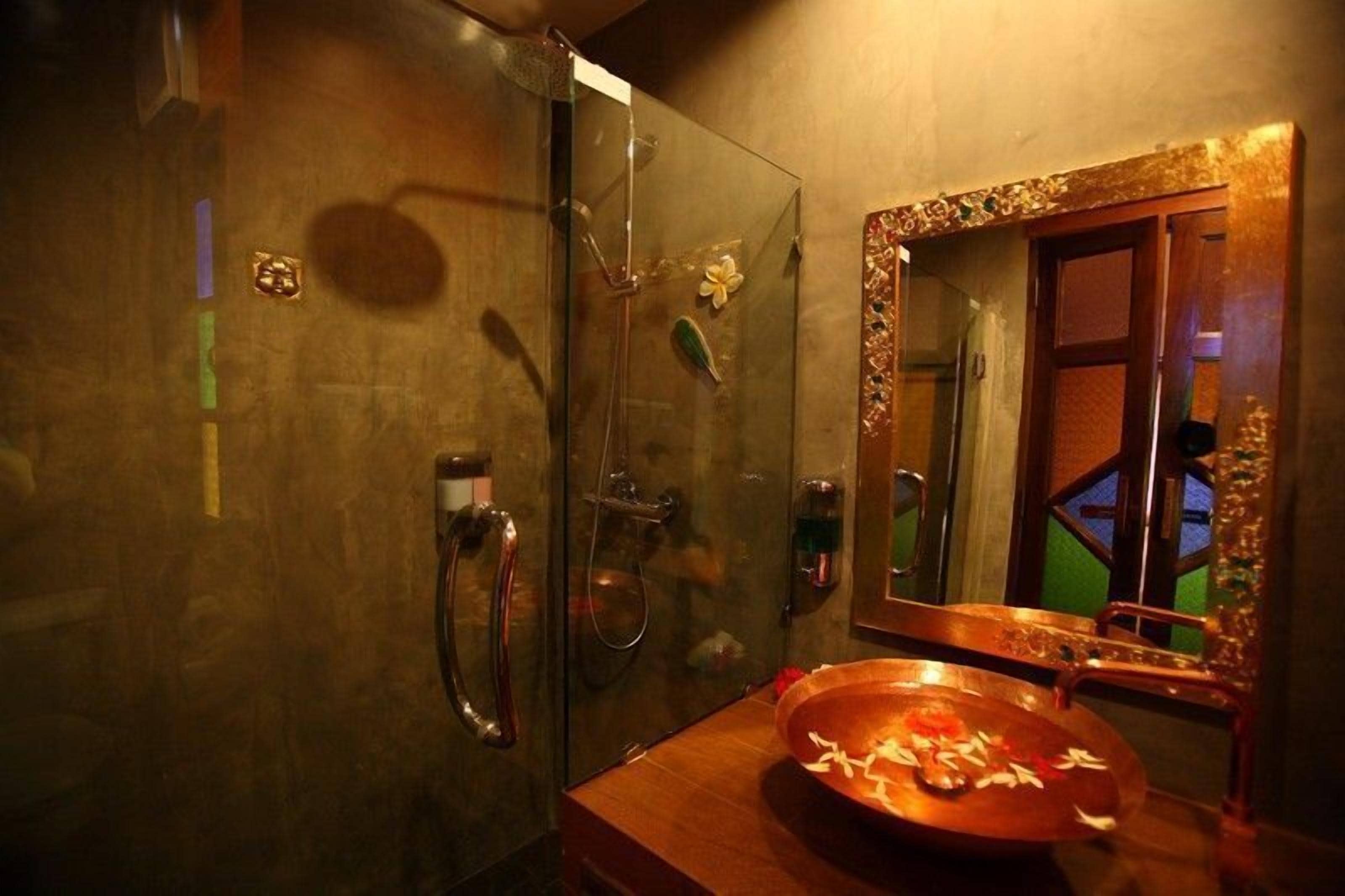 Ein Badezimmer mit Duschkabine aus Glas, einem Holzkosmetikschrank mit Waschbecken und einem Spiegel mit dekorativem Rahmen.