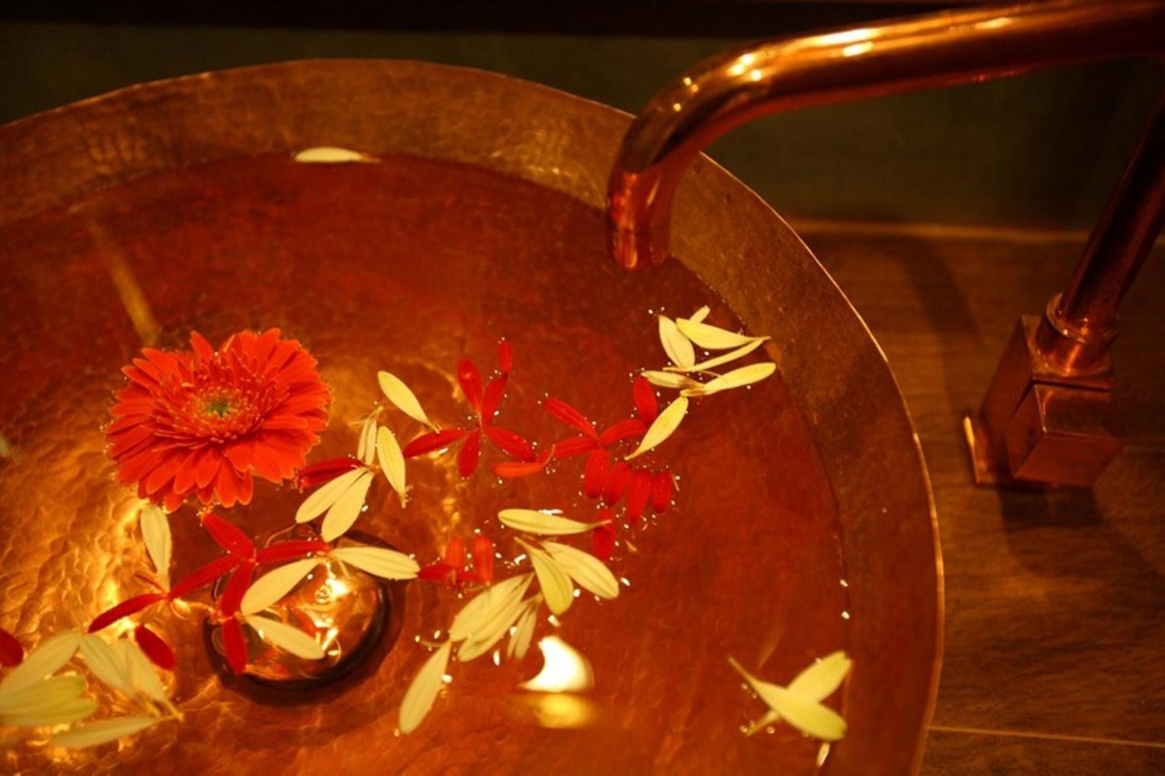 A copper basin with a red flower and white leaves floating in water, with a faucet above.