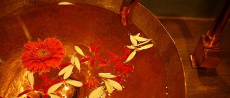 A copper basin with a red flower and white leaves floating in water, with a faucet above.