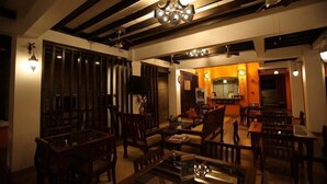 Amplia sala de estar con mobiliario de madera, una cocina al fondo y un techo con vigas y luminarias a la vista.