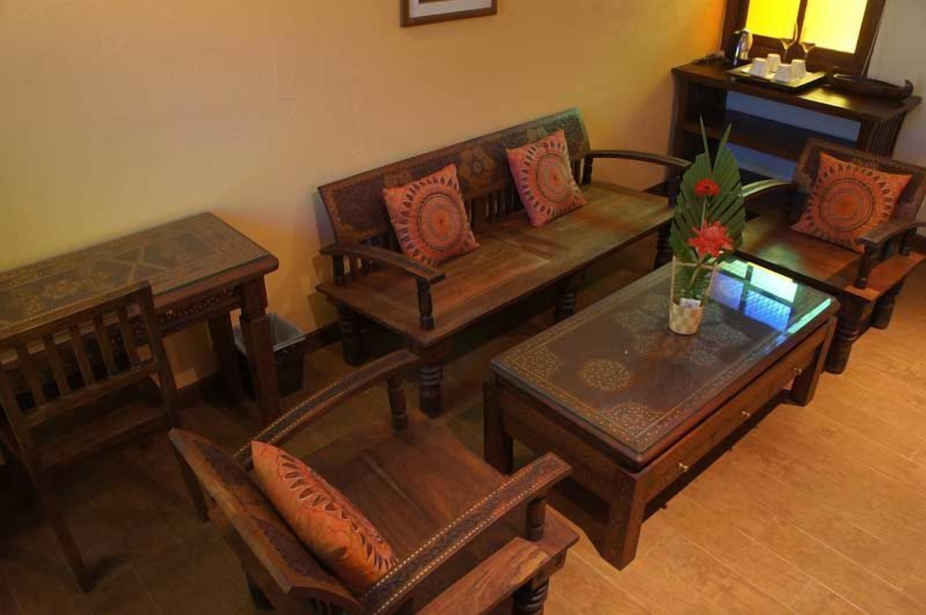 A traditional wooden sofa set with patterned cushions, a matching wooden coffee table, and a small side table.