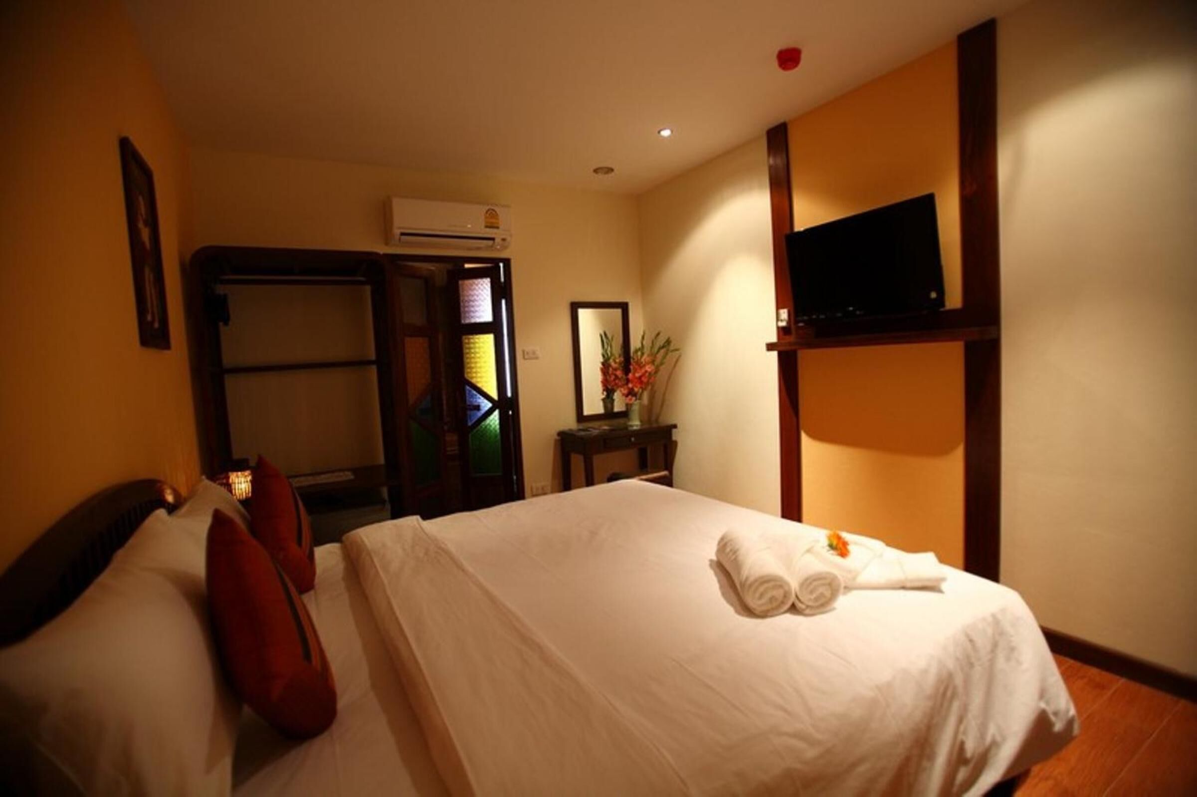 A hotel room with a bed, a TV mounted on the wall, a desk with a chair, and a mirror.