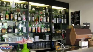 Uma área de bar com prateleiras de garrafas de bebidas, copos e um caixa registradora.