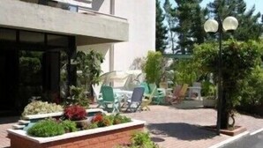 Um edifício moderno com área de entrada pavimentada, mesas ao ar livre e plantas em vasos.