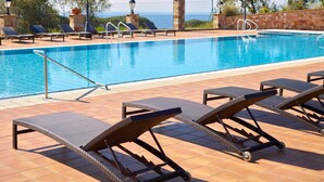 A swimming pool with lounge chairs and a stone wall. - Hapimag Resort Mas Nou (Castell-Platja d'Aro)