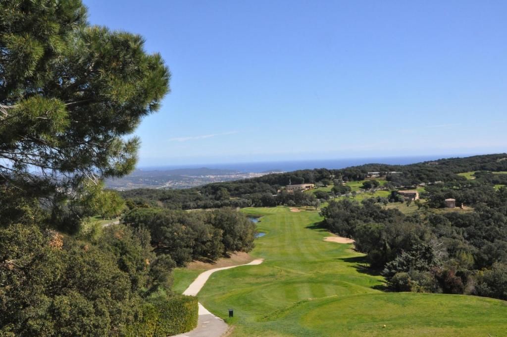 Ein Golfplatz mit freier Bahn, umgeben von dichtem Grün und einem Blick auf eine Stadt in der Ferne.