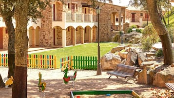 Relax in a serene outdoor space with a lawn, play structures, and a bench amidst large rocks and trees.