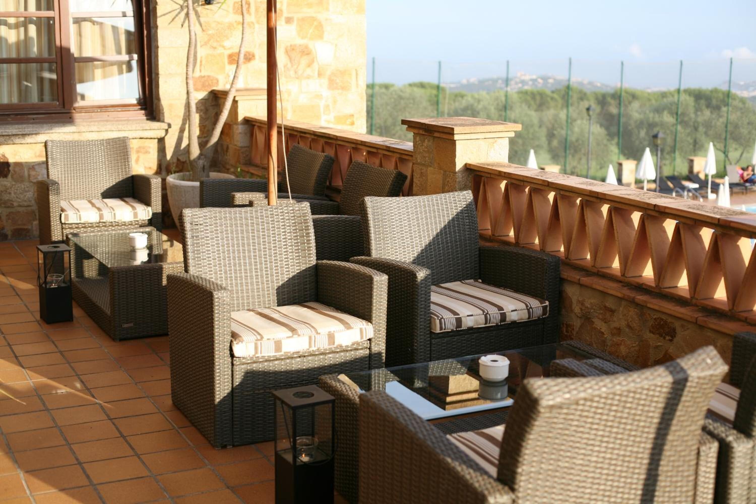 A terrace with wicker furniture and a glass table, overlooking a scenic landscape.
