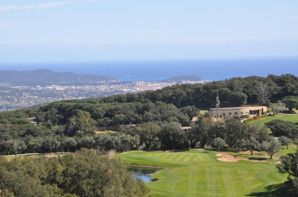 A golf course with a clubhouse, surrounded by trees and hills.