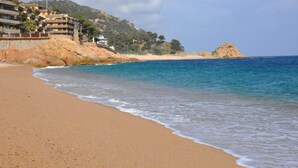 A beach with a rocky outcrop and a building with multiple balconies overlooking the sea. - Hapimag Resort Mas Nou (Castell-Platja d'Aro)
