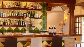 A bar area with multiple shelves of liquor bottles, a decorative metal container, and two bar stools.