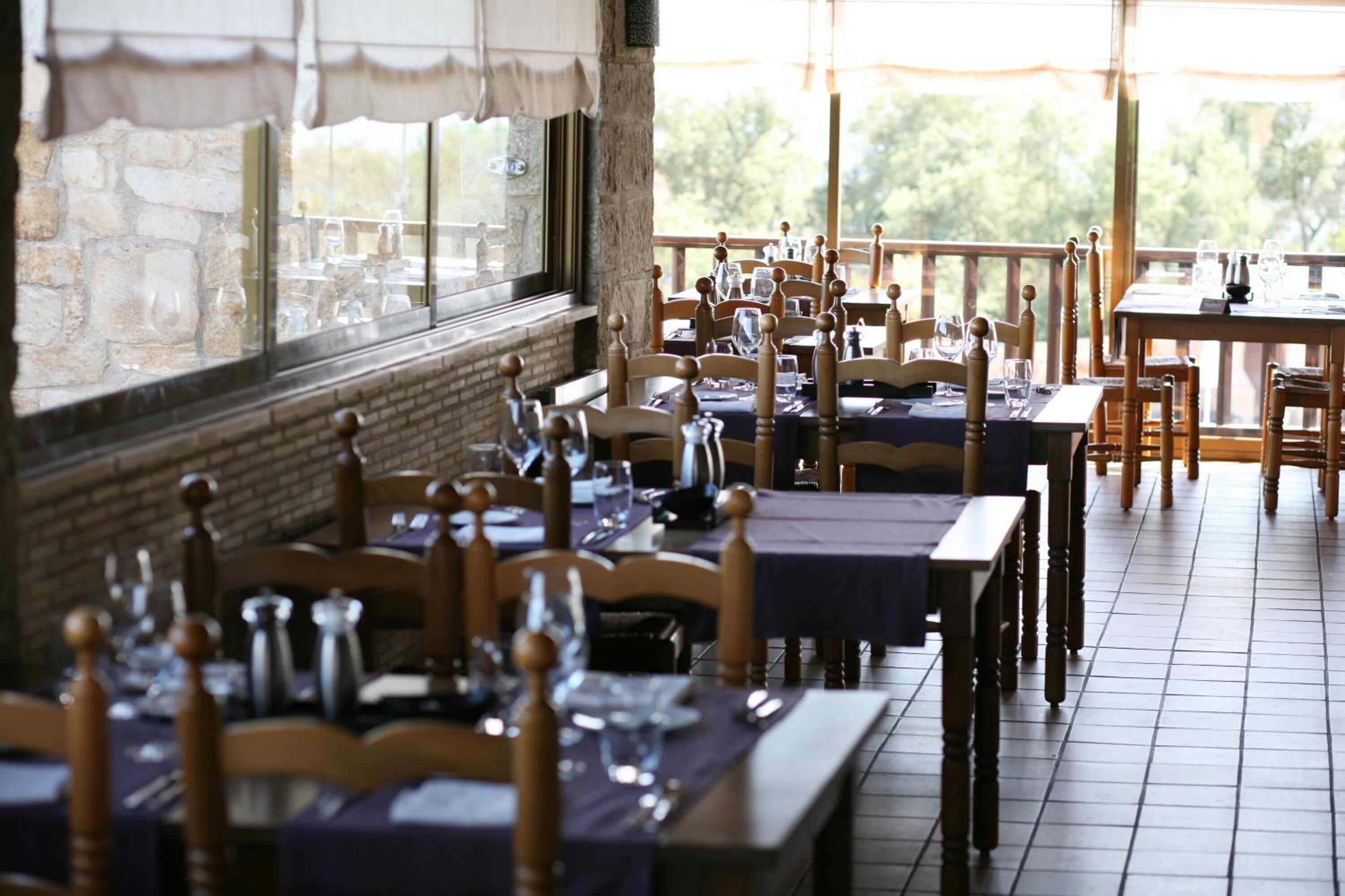 A restaurant with multiple tables and chairs, set against a stone wall and large windows.