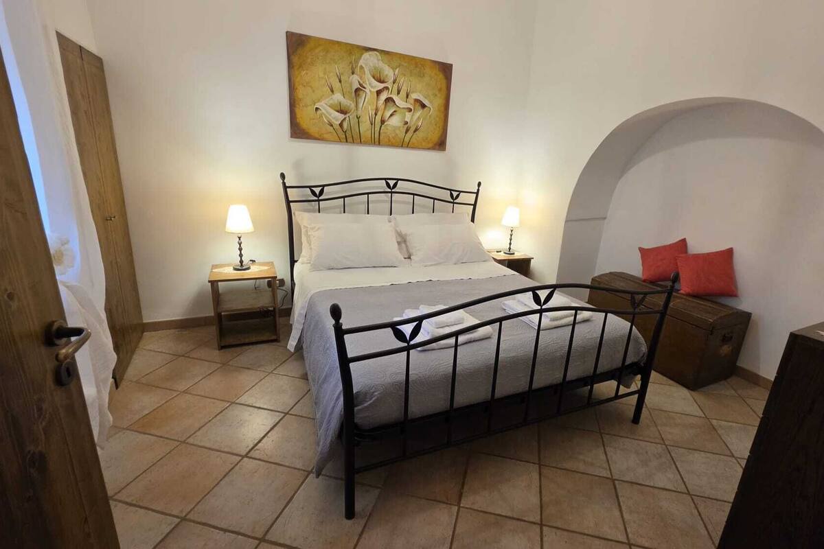 A bedroom with a bed, two bedside tables with lamps, a wooden bench, and a painting on the wall.