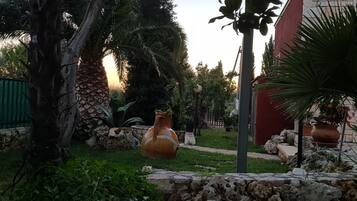 Un jardín con una maceta de terracota grande, un muro de piedra y una palmera.
