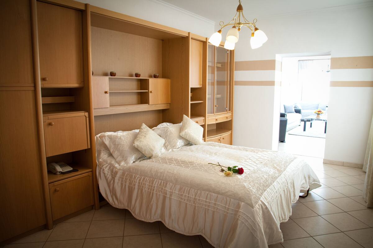 A bedroom with a large bed, wooden built-in shelves, a telephone, and a chandelier.