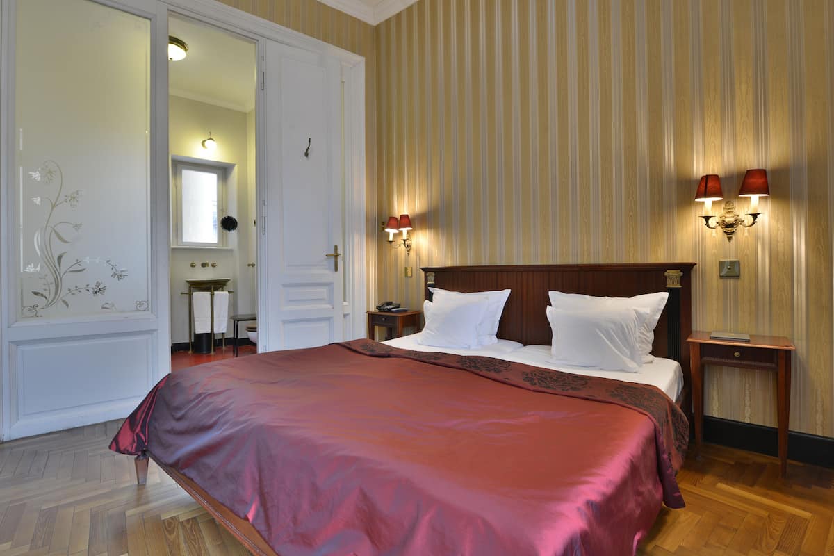 A hotel room with a large bed, two bedside tables, a nightstand, a mirror, and a door leading to a bathroom.