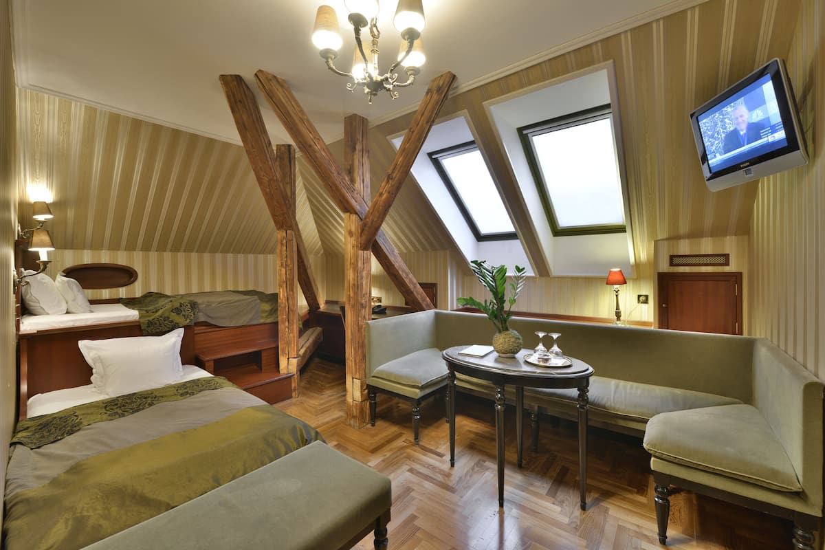 A room with a loft bed, a sofa, a table with a vase, and a television.