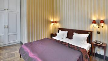 A hotel room with a large bed, a nightstand with a telephone, and two wall-mounted lamps.