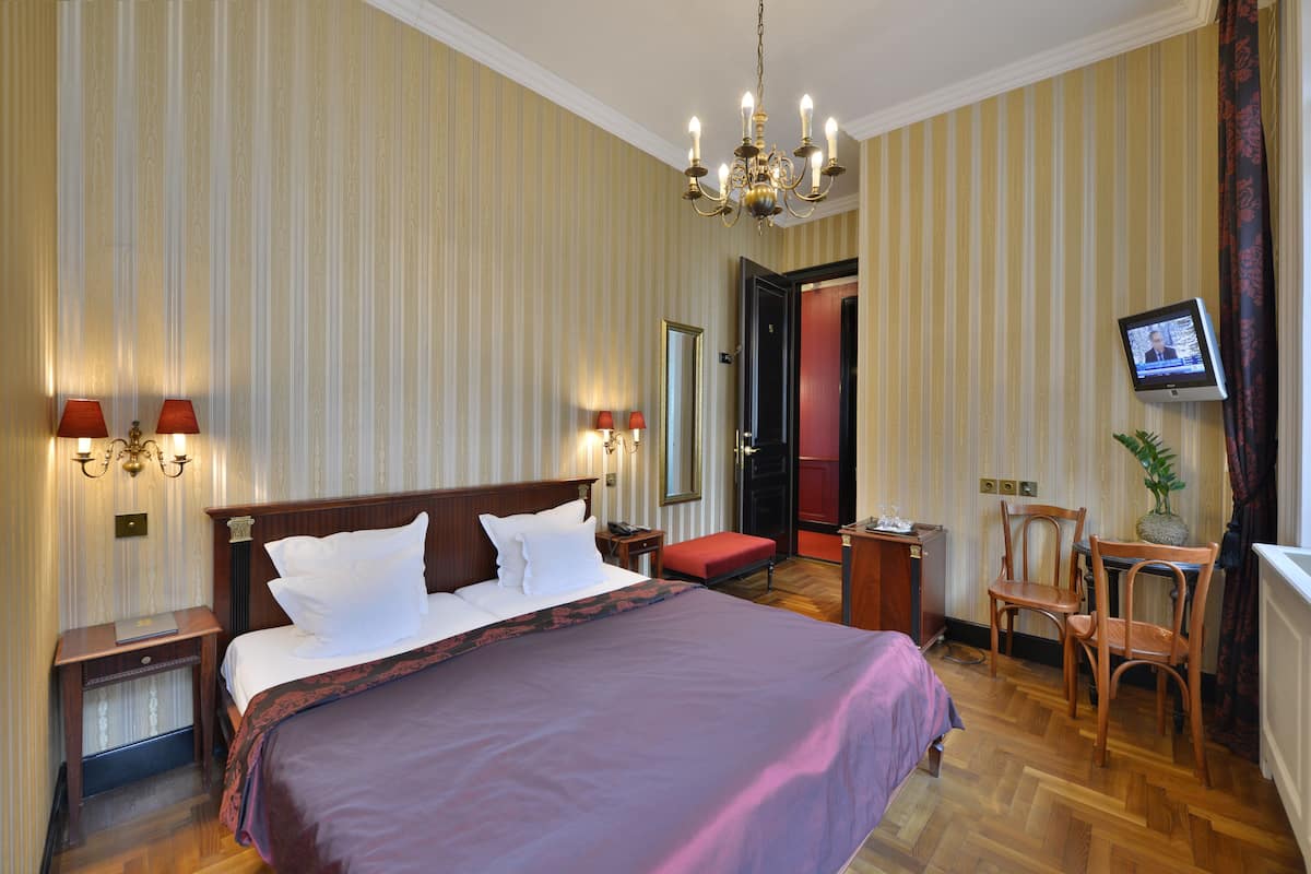 A hotel room with a large bed, bedside lamps, a television, a desk, and a chair.