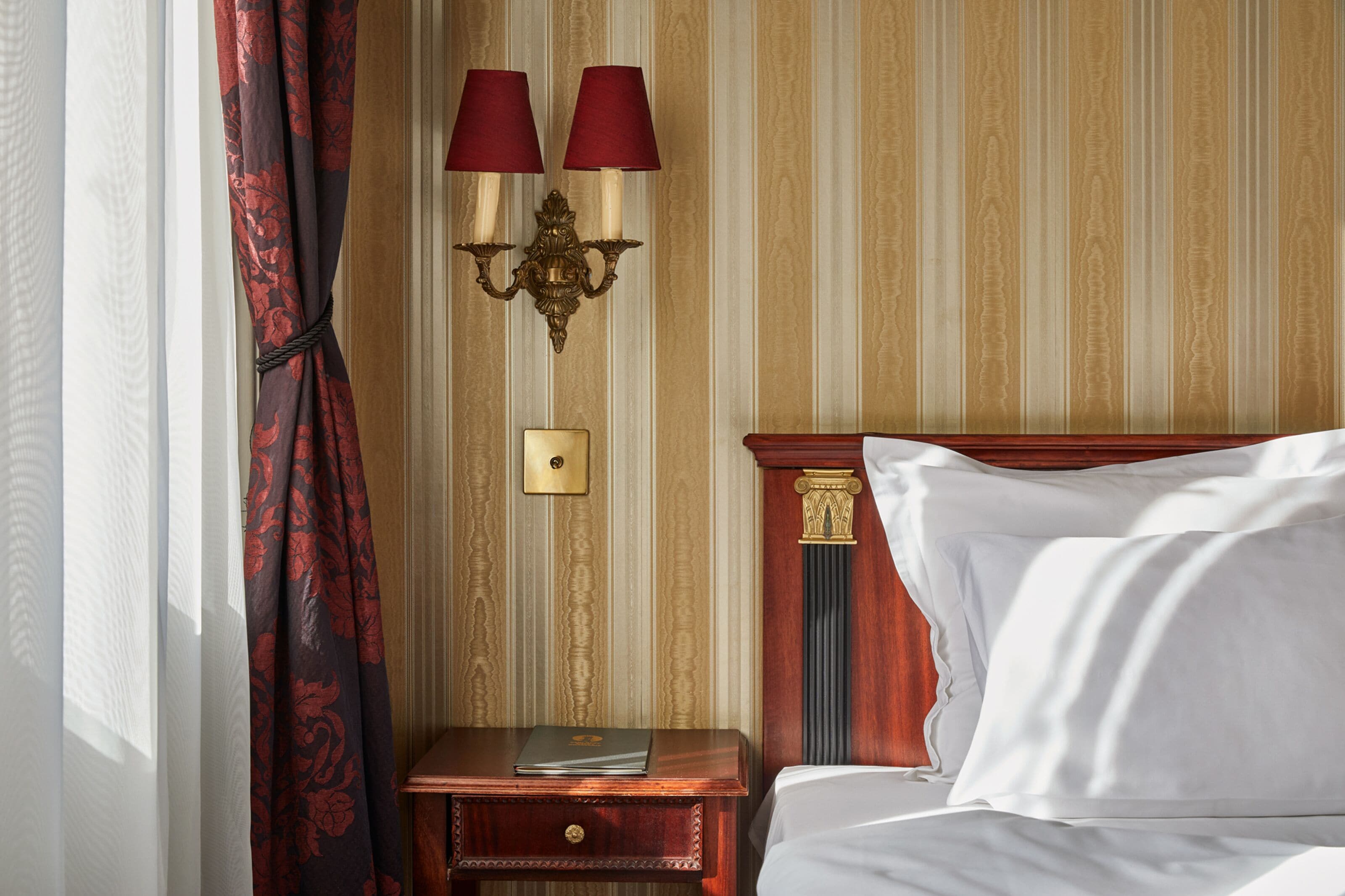 Una habitación de hotel con una cama, una mesita de noche con lámpara y una ventana con cortinas.