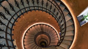 A spiral staircase with ornate metal railings and a copper-colored wall. - Gerlóczy Boutique Hotel (Budapest)