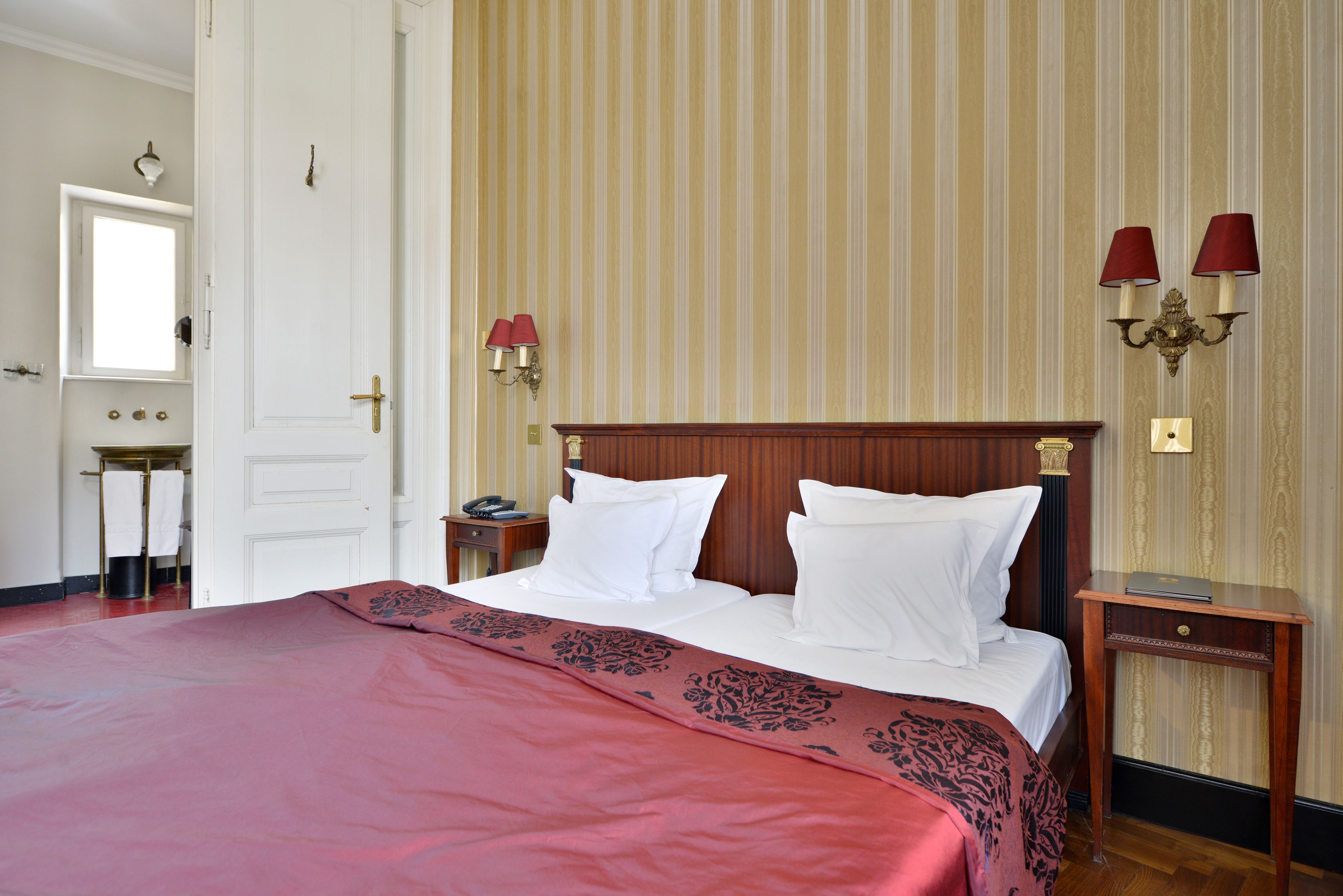 Une chambre d’hôtel avec un grand lit, une tête de lit en bois, une table de chevet et une lampe fixée au mur.