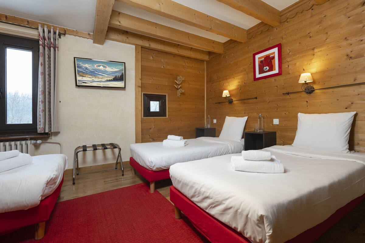 Ein Hotelzimmer mit zwei Betten, einer Holzbalkendecke, einem Gemälde, einer Lampe und einem Fenster mit Vorhängen.
