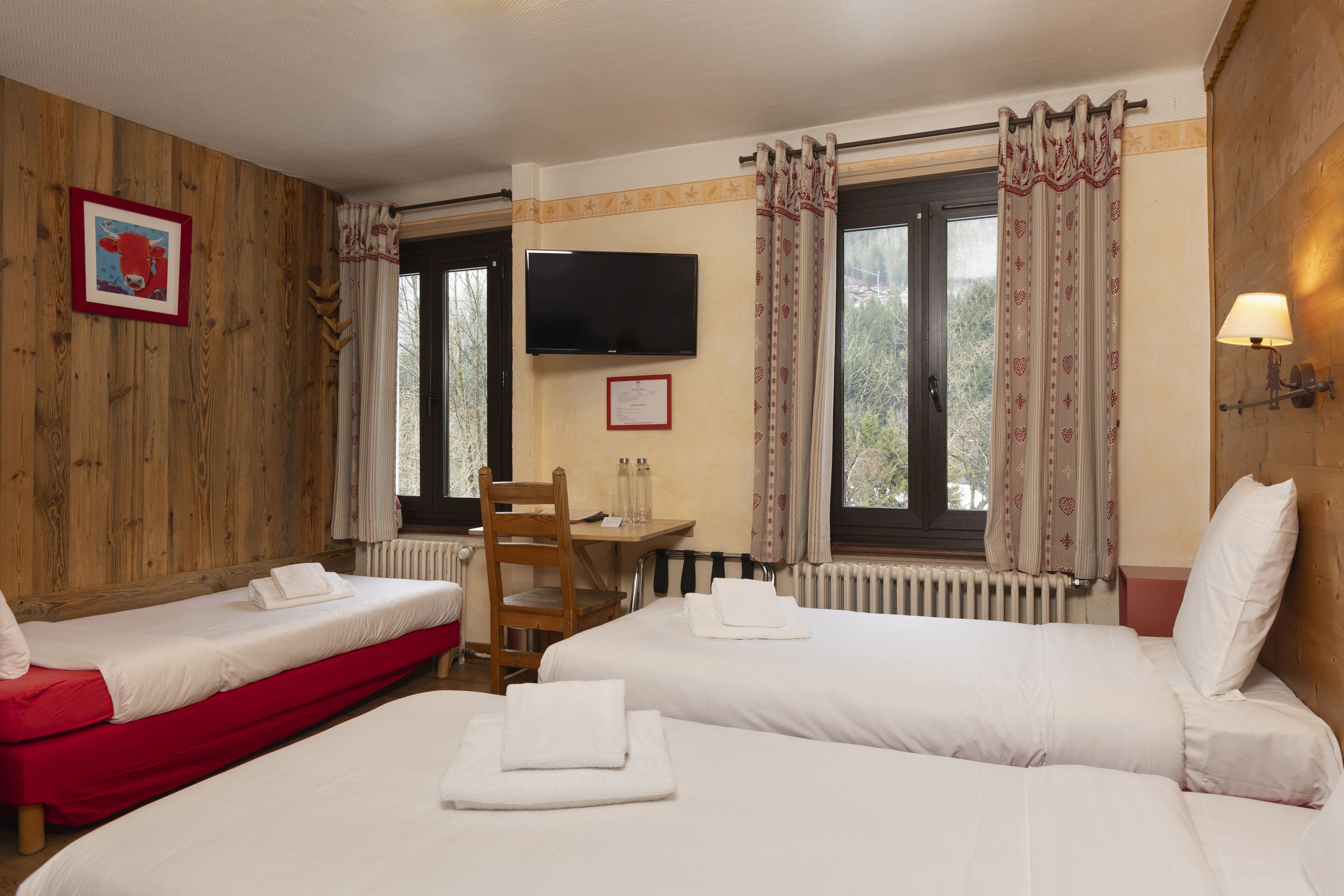 A hotel room with two beds, a wooden wall, a TV, a desk, and a window with curtains.