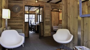 Een modern interieur met houten wanden, twee witte stoelen, een bureau en een klok.