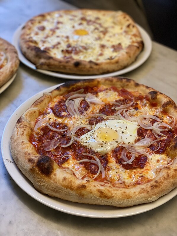 Deux pizzas garnies et un œuf au plat sur l’une d’elles.