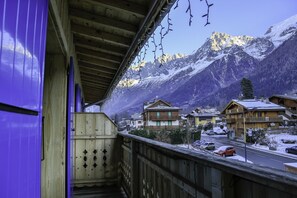 Un balcón de madera con vistas a un pueblo montañoso nevado, con casas tradicionales y un cielo despejado.