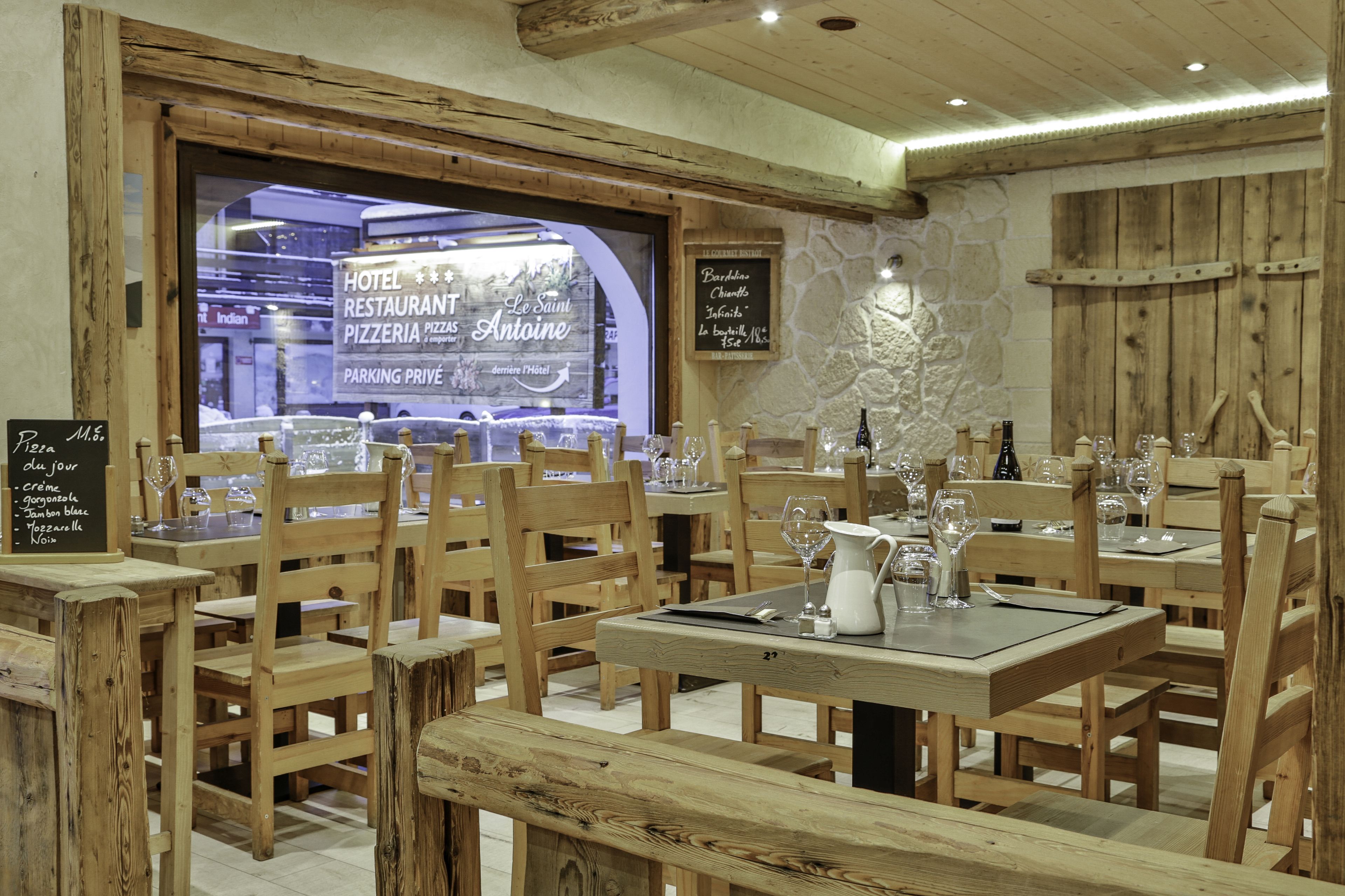 A restaurant with wooden furniture and a stone wall. Tables are set with wine glasses and menus.