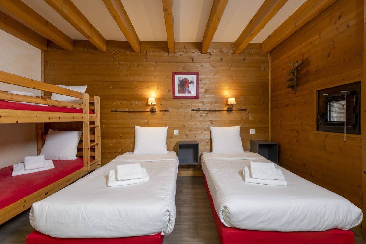 Ein Zimmer mit zwei Einzelbetten, einem Etagenbett, Holzwänden und zwei Wandlampen.