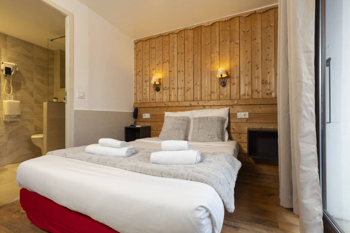 Ein Hotelzimmer mit hölzernem Kopfteil, einem Bett mit weißen Leinen und Handtüchern, einem Nachttisch und einem Holzboden.