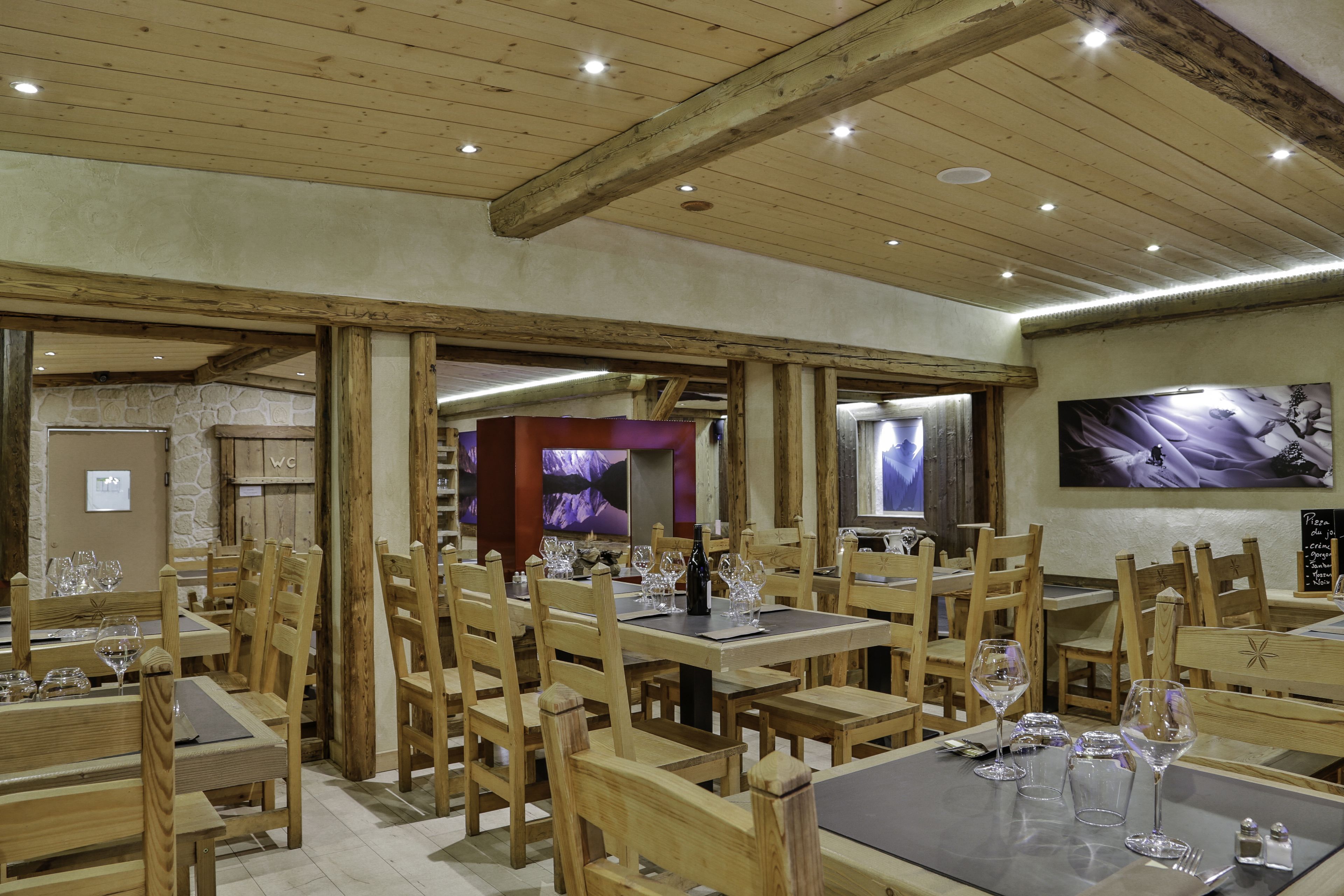 A restaurant with wooden tables and chairs, wine glasses, and a stone wall.