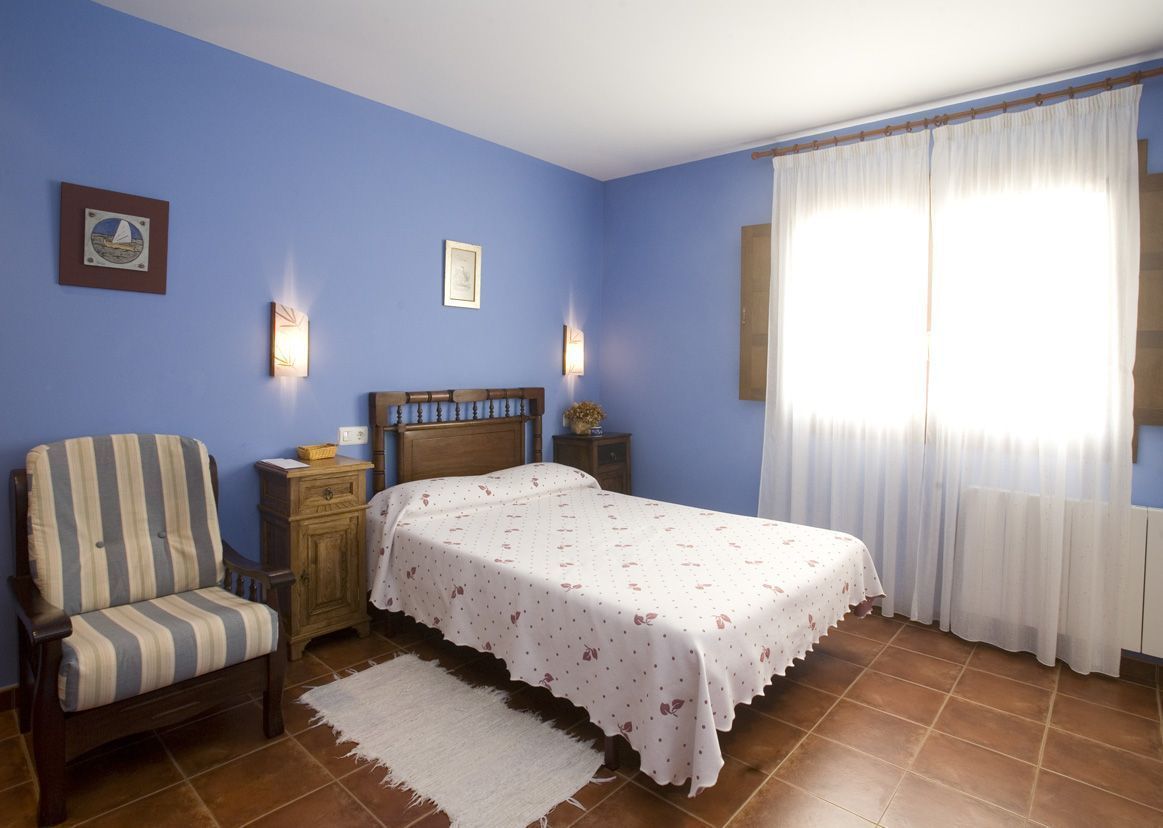 A bedroom with a bed, a chair, a nightstand, and a window with curtains.