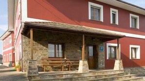 A red building with a stone porch and wooden benches. - Turismo Rural Suquin (Navia)