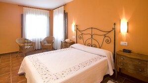 A bedroom with a bed, two chairs, a nightstand, and two wall-mounted lamps. - Turismo Rural Suquin (Navia)