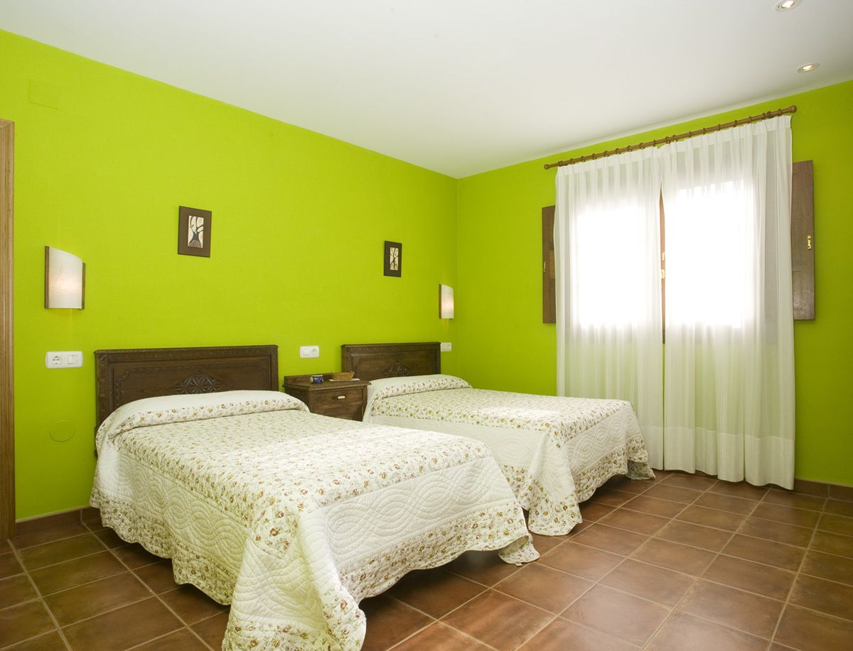 A room with two beds, green walls, and a window with white curtains.