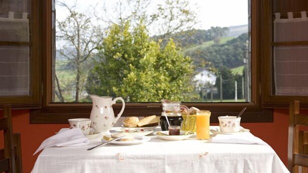 A breakfast table with various items and a view of a green landscape through a window. - Turismo Rural Suquin (Navia)