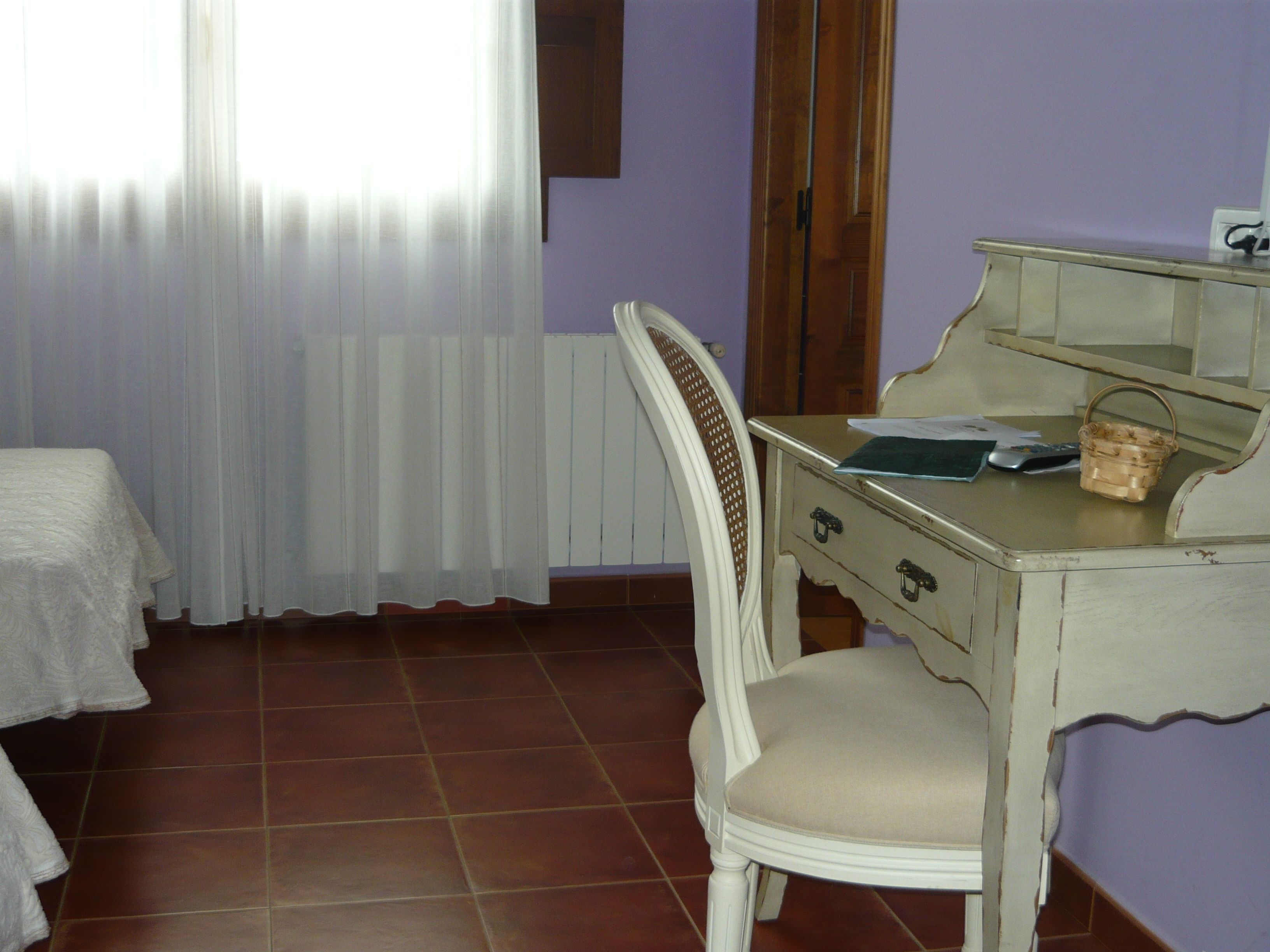 Una habitación con cama, escritorio y silla, ventana con cortinas y radiador.