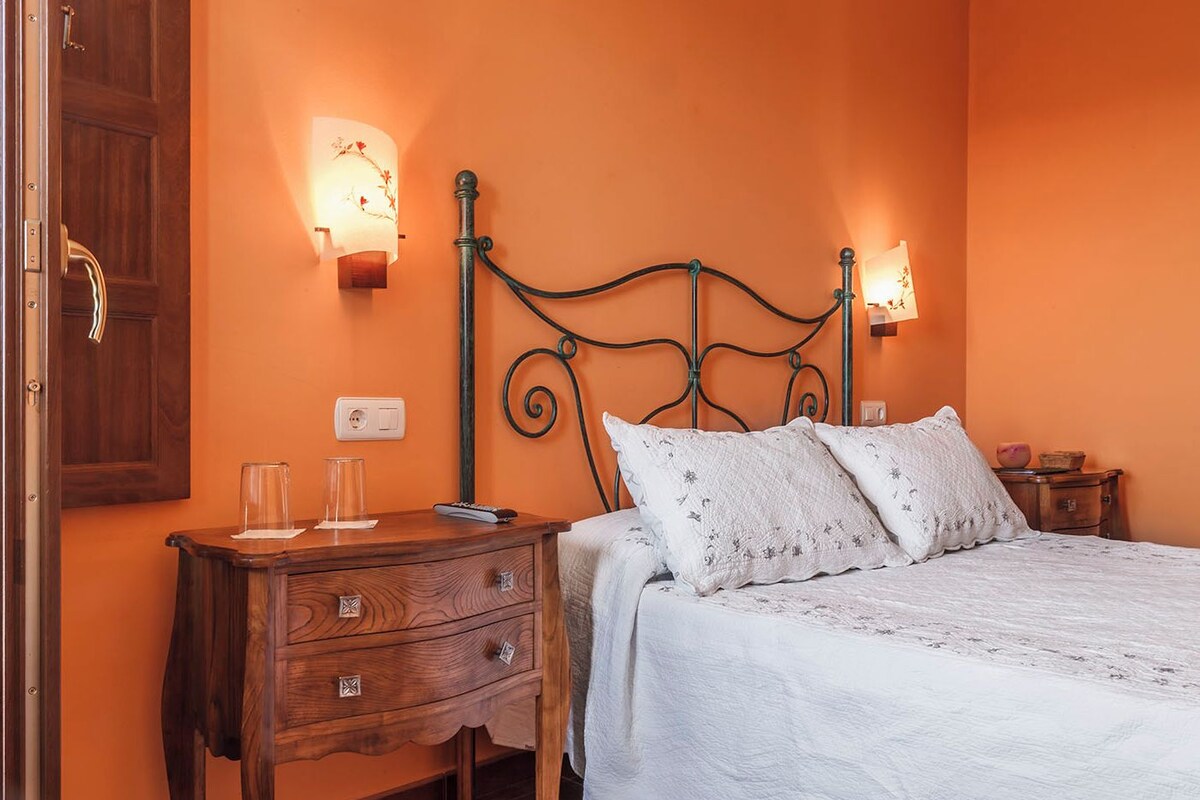 A bedroom with a wooden nightstand, a bed with white bedding, and two wall-mounted lamps.